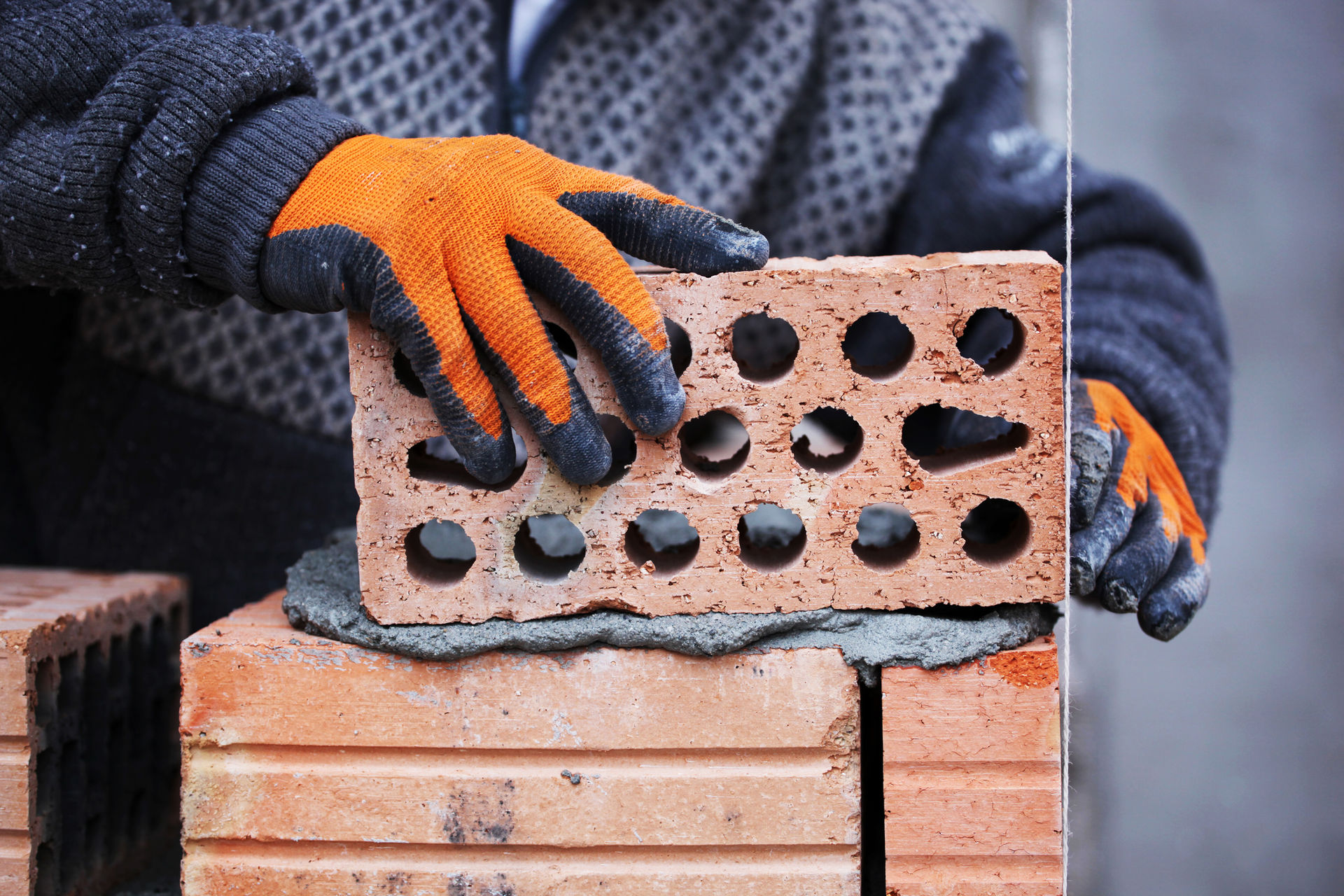 Gloved hands laying a single brick, close up on the joint