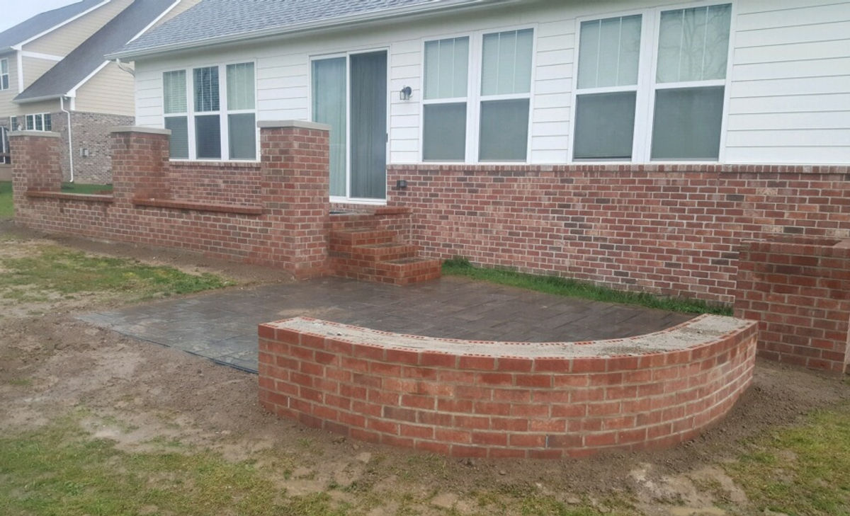 Restored brick paver patio and brick seat wall beside a home
